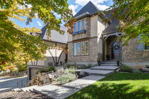 View of front facade featuring a garage, stone siding, stucco siding, and a front lawn