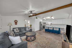 Living room featuring ceiling fan, lofted ceiling with skylight, sink, and light hardwood / wood-style flooring