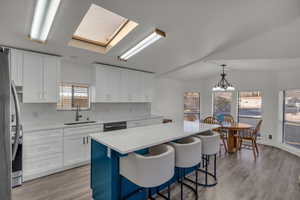 Kitchen with sink, white cabinetry, decorative backsplash, a kitchen island, and decorative light fixtures