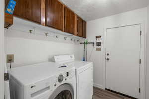 Clothes washing area featuring dark wood-type flooring, cabinets, washing machine and dryer, and a textured ceiling