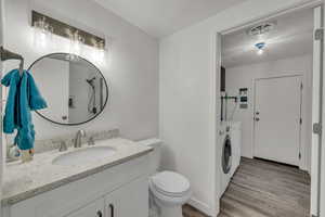 Bathroom featuring hardwood / wood-style floors, washing machine and dryer, vanity, a textured ceiling, and toilet