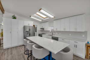 Kitchen with white cabinetry, stainless steel appliances, lofted ceiling with skylight, and a center island