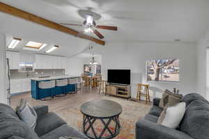 Living room featuring ceiling fan with notable chandelier, sink, vaulted ceiling with skylight, and light wood-type flooring