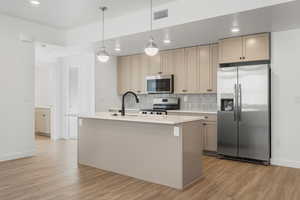 Kitchen with tasteful backsplash, hanging light fixtures, a center island with sink, appliances with stainless steel finishes, and light hardwood / wood-style floors