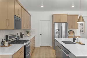 Kitchen with sink, appliances with stainless steel finishes, pendant lighting, light stone countertops, and backsplash