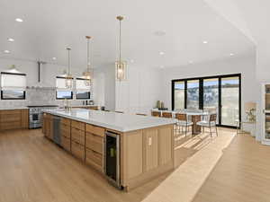 Kitchen featuring a large island, appliances with stainless steel finishes, hanging light fixtures, wine cooler, and wall chimney exhaust hood