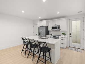 Kitchen featuring a kitchen bar, sink, white cabinetry, appliances with stainless steel finishes, and an island with sink