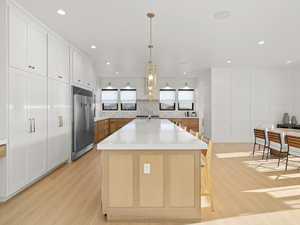 Kitchen featuring a spacious island, white cabinetry, stainless steel built in fridge, pendant lighting, and light hardwood / wood-style floors
