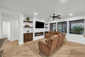 Living room featuring built in shelves, light hardwood / wood-style flooring, a large fireplace, and ceiling fan