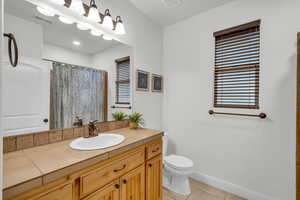 Bathroom with curtained shower, toilet, vanity, and tile patterned flooring