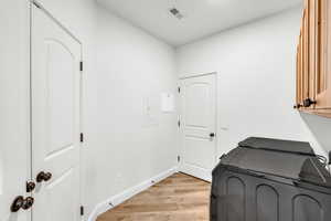 Washroom with cabinets, light hardwood / wood-style flooring, and washing machine and dryer