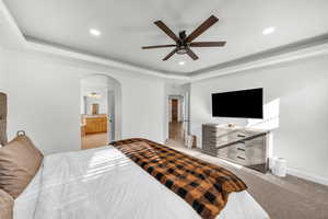 Carpeted bedroom with ceiling fan, ensuite bathroom, and a tray ceiling