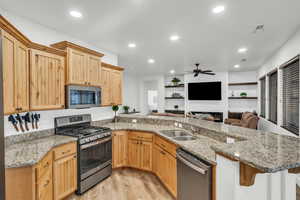 Kitchen featuring kitchen peninsula, sink, light stone countertops, and appliances with stainless steel finishes