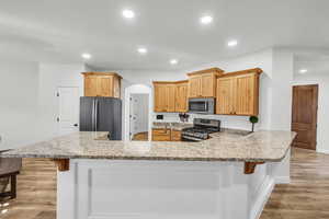 Kitchen with light wood-type flooring, a breakfast bar area, kitchen peninsula, and appliances with stainless steel finishes