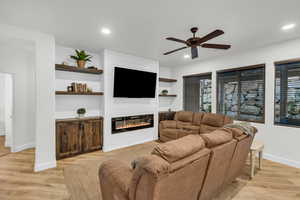 Living room featuring a large fireplace, built in shelves, ceiling fan, and light hardwood / wood-style floors