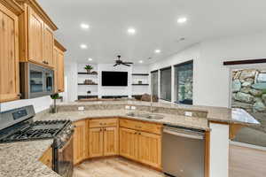 Kitchen with light hardwood / wood-style floors, sink, kitchen peninsula, stainless steel appliances, and light stone counters