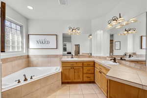 Bathroom featuring tile patterned flooring, tiled bath, and vanity