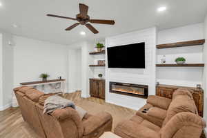 Living room with ceiling fan, a large fireplace, and light hardwood / wood-style flooring