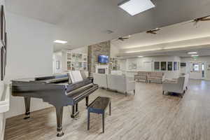 Misc room with a stone fireplace, vaulted ceiling, built in shelves, light hardwood / wood-style flooring, and ceiling fan