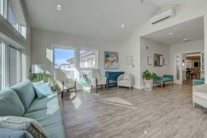 Living room featuring high vaulted ceiling, light hardwood / wood-style flooring, and a wall mounted AC