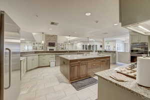Kitchen featuring stainless steel appliances, a large island, light stone countertops, and decorative light fixtures