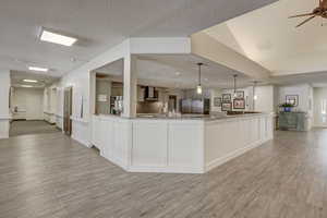 Kitchen featuring light stone countertops, white cabinets, decorative light fixtures, wall chimney exhaust hood, and stainless steel fridge