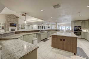 Kitchen featuring hanging light fixtures, a spacious island, appliances with stainless steel finishes, light stone countertops, and a textured ceiling