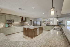Kitchen with appliances with stainless steel finishes, a kitchen island with sink, sink, pendant lighting, and wall chimney exhaust hood