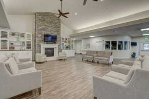 Living room with light wood-type flooring, ceiling fan, a stone fireplace, and high vaulted ceiling