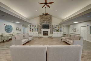Living room featuring ceiling fan, vaulted ceiling, a stone fireplace, and light wood-type flooring