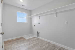 Laundry area with light hardwood / wood-style flooring, hookup for a washing machine, a textured ceiling, and electric dryer hookup