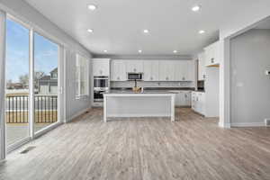 Kitchen featuring appliances with stainless steel finishes, an island with sink, light wood-type flooring, white cabinets, and a textured ceiling