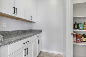 Bar with light stone counters, light hardwood / wood-style flooring, and white cabinets