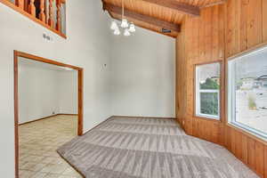 Empty room featuring high vaulted ceiling, wood walls, beamed ceiling, wooden ceiling, and an inviting chandelier