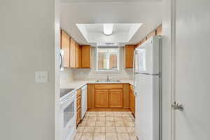 Kitchen with sink, white appliances, and a tray ceiling