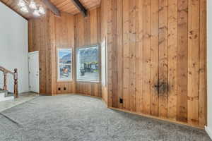 Carpeted spare room with high vaulted ceiling, wood ceiling, beam ceiling, and wood walls