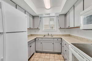 Kitchen featuring a raised ceiling, sink, gray cabinetry, and white appliances