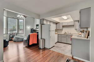 Kitchen with gray cabinetry, sink, white appliances, and light wood-type flooring