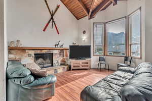 Living room featuring hardwood / wood-style flooring, a stone fireplace, wood ceiling, and lofted ceiling with beams