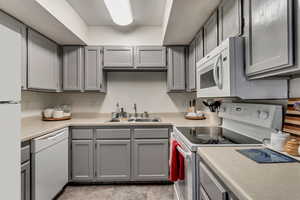 Kitchen featuring gray cabinetry, sink, and white appliances