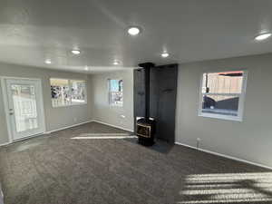 Unfurnished living room featuring dark carpet, a textured ceiling, and a wood stove