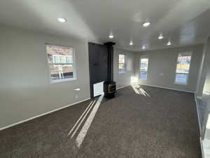 Interior space featuring dark colored carpet, a wood stove, and a textured ceiling