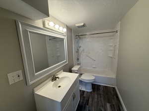 Full bathroom with tiled shower / bath combo, vanity, wood-type flooring, a textured ceiling, and toilet