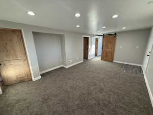 Unfurnished bedroom featuring a barn door and dark carpet