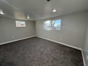 Basement with plenty of natural light, a textured ceiling, and dark colored carpet