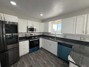 Kitchen with stainless steel appliances, sink, dark stone countertops, and white cabinets