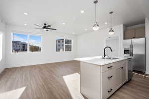 Kitchen with decorative light fixtures, sink, light hardwood / wood-style floors, stainless steel appliances, and a center island with sink