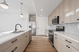 Kitchen featuring sink, tasteful backsplash, decorative light fixtures, stainless steel appliances, and light hardwood / wood-style floors