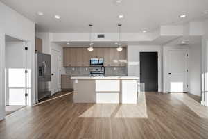 Kitchen with decorative backsplash, stainless steel appliances, hanging light fixtures, and a center island with sink