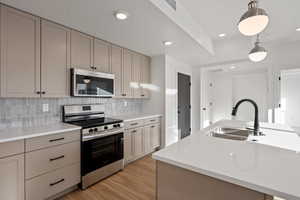 Kitchen featuring appliances with stainless steel finishes, decorative light fixtures, sink, backsplash, and a kitchen island with sink